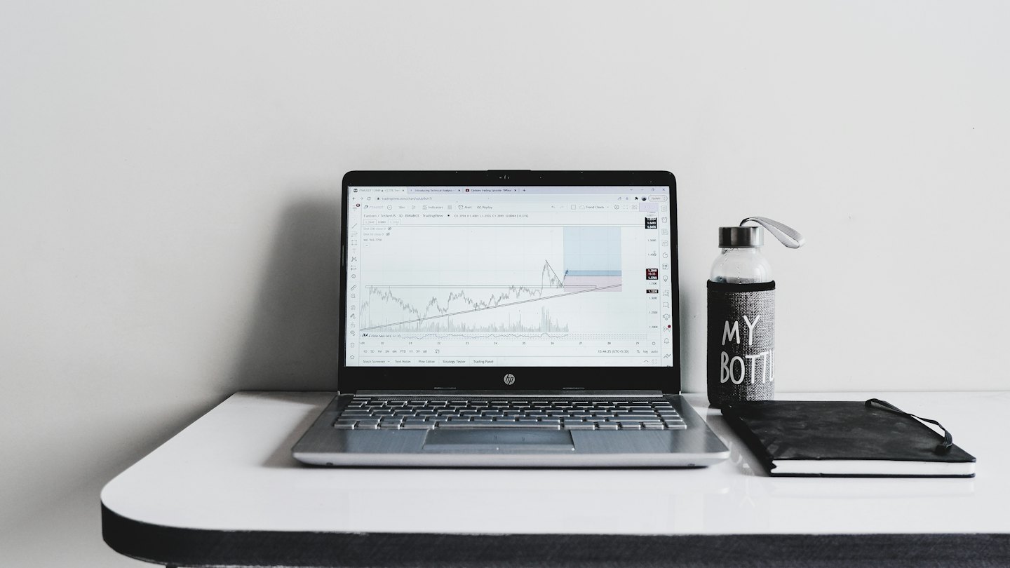 Laptop met financiële grafieken naast een notitieboekje en waterfles.